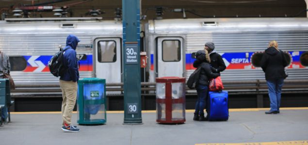 An image of travelers with suitcases and duffle bags waiting on a train platform with a Southeastern Pennsylvania Transit Authority train in the background